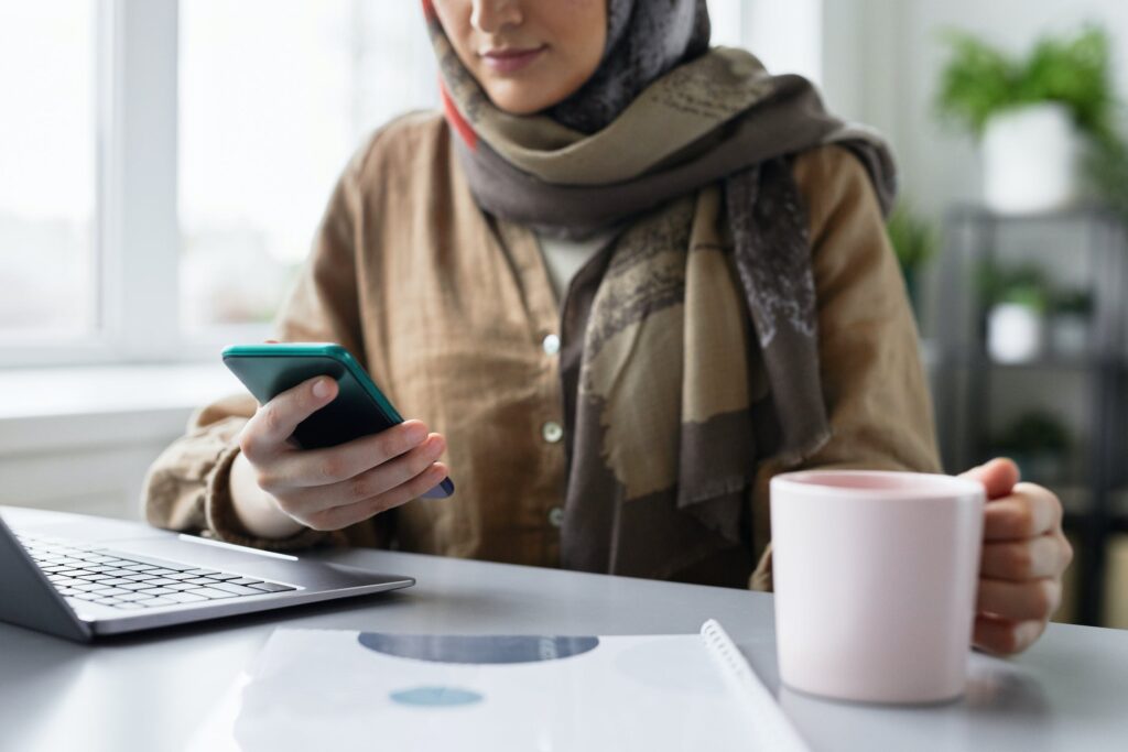 Muslim woman working at her desk while using handphone