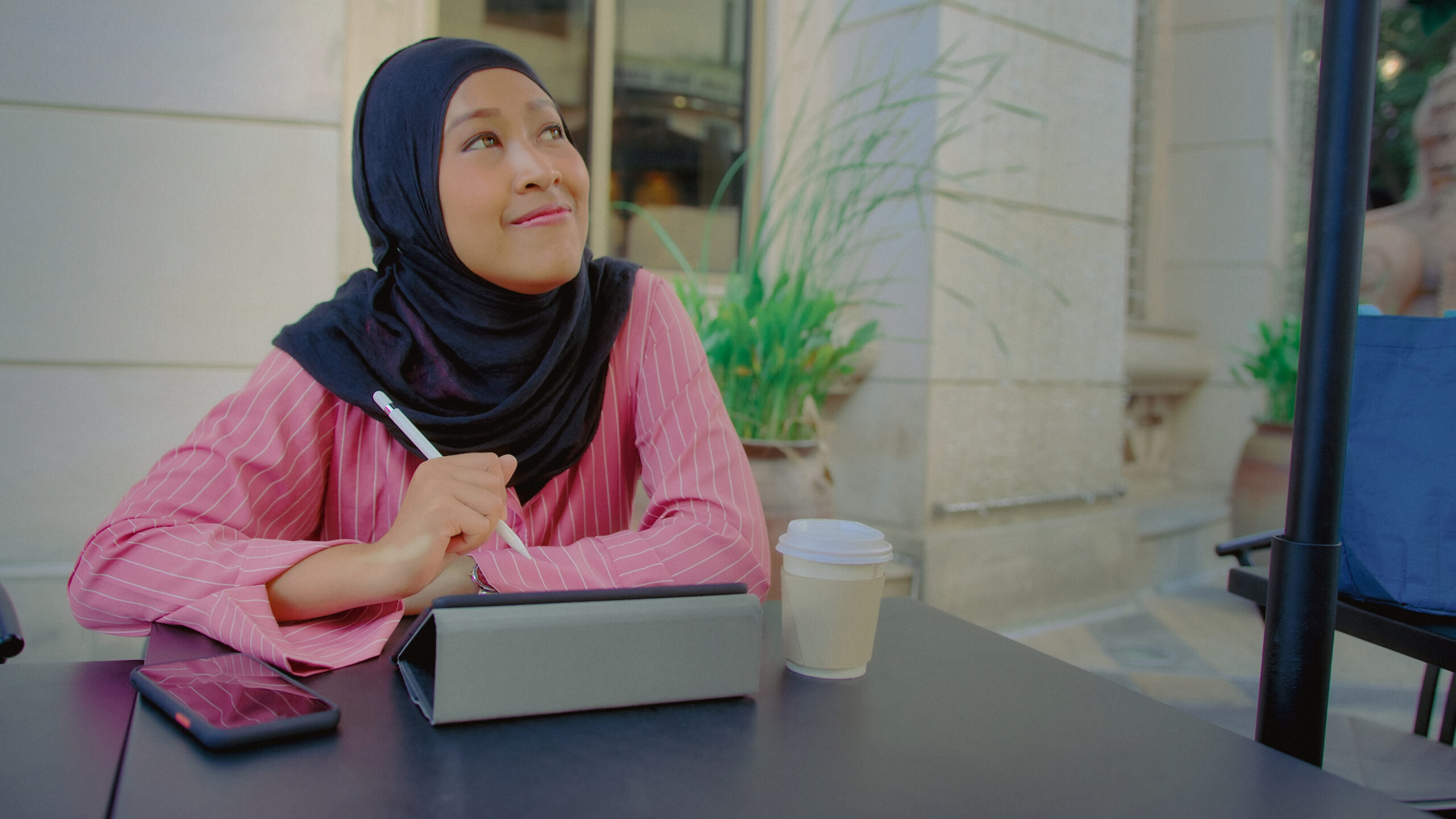 muslim woman thinking and journaling on her tablet