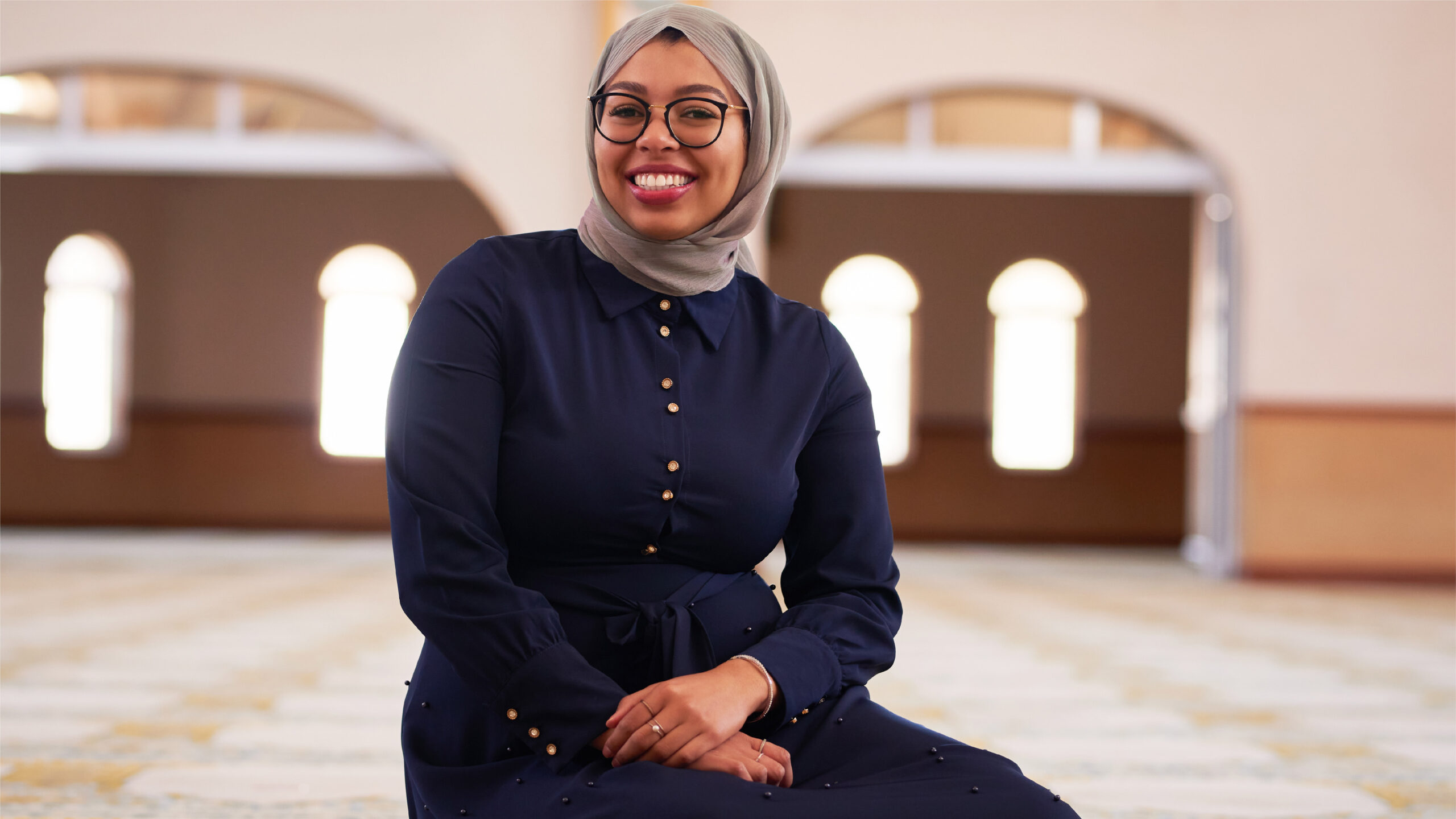 Muslim Woman sitting in a blue dress with a hijab and smiling