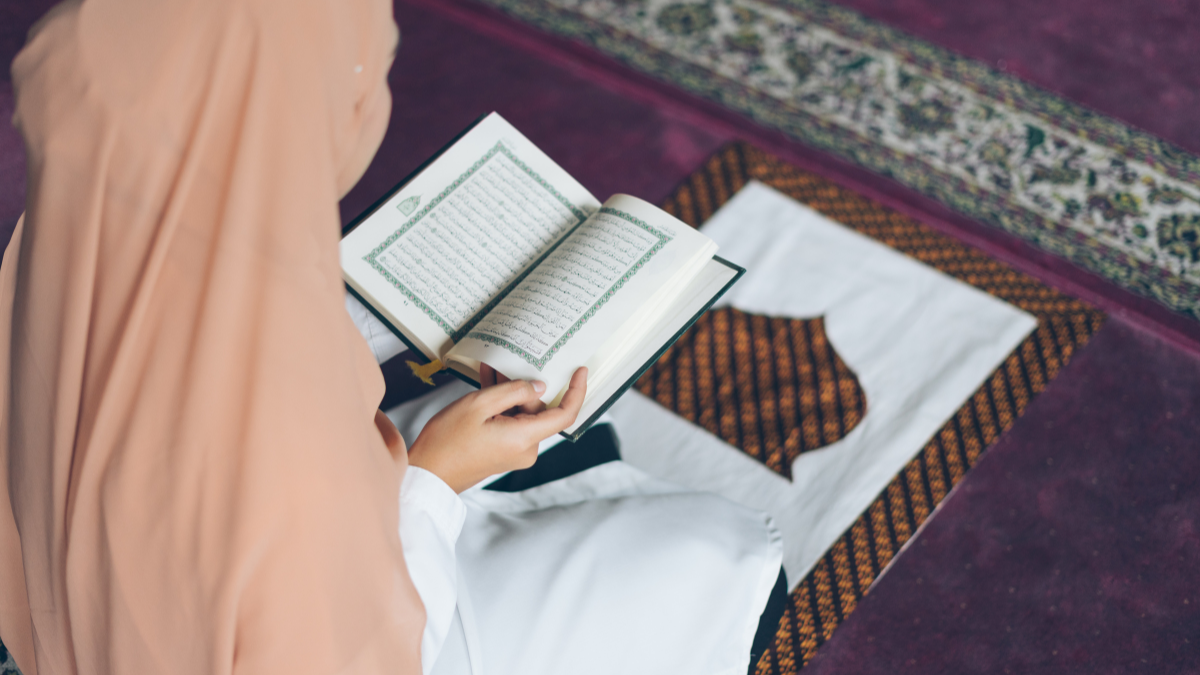 muslim woman reading the quran on prayer mat